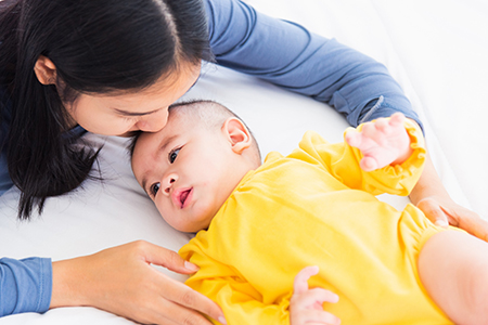 Portrait of beautiful young Asian mother kissing her infant newborn baby in a white bed