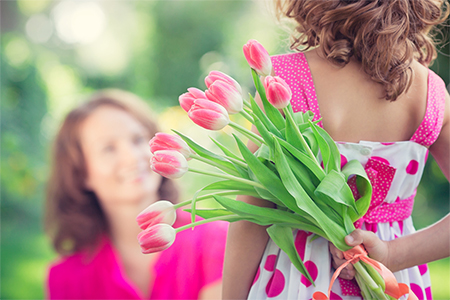 concept - Women's day; Woman and child with bouquet of flowers against green blurred background