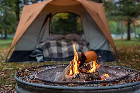 Closeup of campfire in evening with cozy orange tent in background