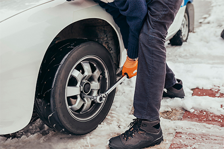 Mechanic wearing orange gloves and winter clothes, changing car wheel