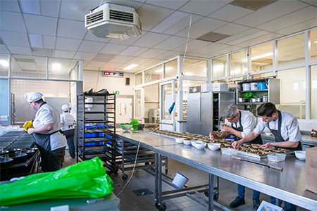 Chefs preparing food in a commercial kitchen with stainless steel equipment