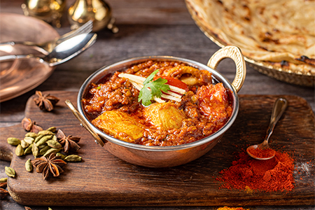 A copper plate with curry and veggies on a wooden board