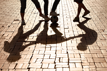 Kicking it with some friends. Cropped image of legs kicking a ball with shadows on the paved road