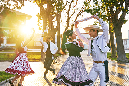 group of four  adults dressed as huaso dancing cueca in the town square at sunset