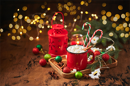 Red cup of hot cocoa with marshmallows and candy canes on wooden table with christmas tree