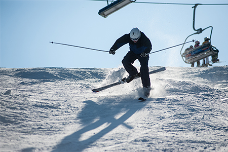 Skier in the moment of falling on the snowy slope with a ski lifts and blue sky
