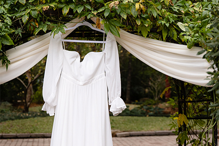 A white wedding dress hangs off the side of a beautiful ceremony arch