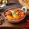 A copper plate with curry and veggies on a wooden board