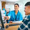 Female Nurse Or Doctor Wearing Scrubs At Hospital Appointment With Male Patient Looking At Computer