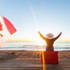 concept - woman tourist sitting near the sea on the red suitcase and in hat and watching sunset and 