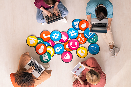 Top view of four young friendly people in casualwear sitting by multi-color papers with icons on the