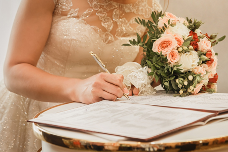 Bride's hand puts signature pen on consent to marry at wedding close-up.