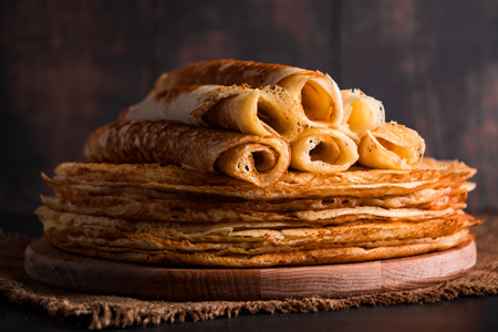 Traditional Russian food - thin pancakes. A stack of crepes on a dark brown wooden background. Rusti