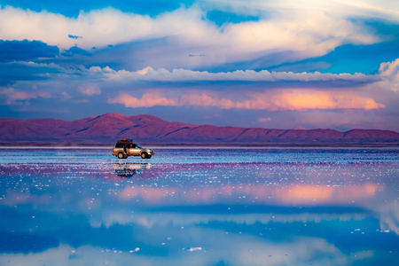 Car standing in middle of salt flat reflecting blue sky, Salar de Uyuni, Bolivia