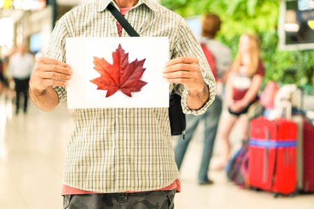 man waiting at airport with sign showing maple leaf