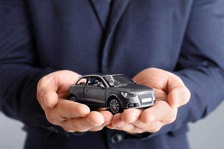 Male insurance agent holding toy car on grey background, closeup