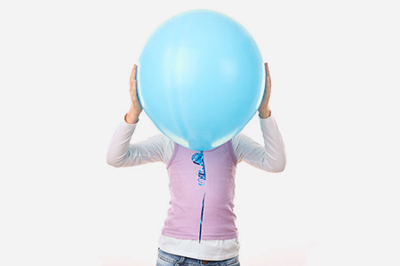 Studio portrait of little girl hiding behind blue balloon against white background