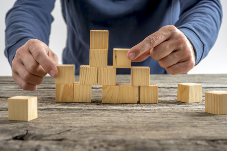 Close up Man Assembling a Tower Using Wooden Cubes on Top of a Rustic Table.