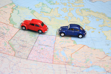 Miniature red and blue toy cars driving in tandem on a map of canada