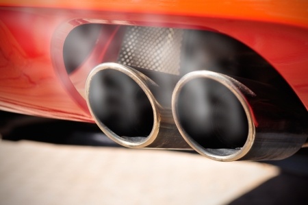 Close up of red car tailpipe showing exhaust smoke