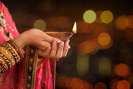 Close up Indian woman in traditional sari lighting oil lamp and celebrating Diwali or deepavali, fes