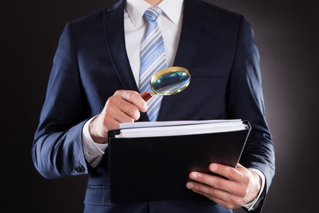 Midsection of person in suit examining documents with magnifying glass against black background