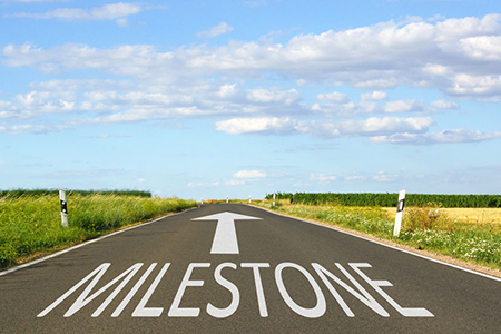 Milestones written on road with arrow