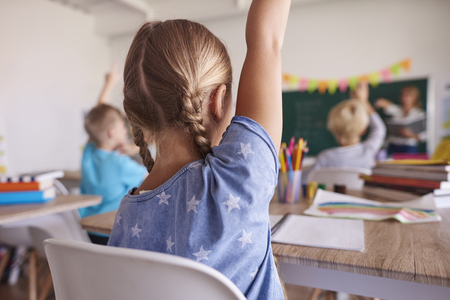 back view of young girl in classroom raising hand