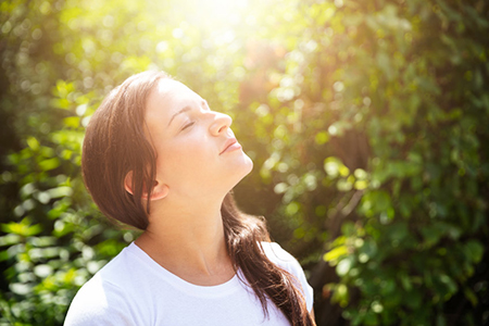 Woman smelling the fresh air outside. Background trees and sunshine