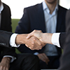 Close up view of two businessmen in suits shake hands at group meeting, business partners handshakin