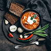 Traditional Ukrainian Russian red soup borscht with ingredients, spice and herbs in the bowl on a da
