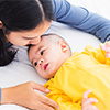 Portrait of beautiful young Asian mother kissing her infant newborn baby in a white bed