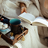 happy young female in knitted cosy cardigan with tray and cup reading book in the modern living room