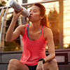 sporty woman sitting outdoors resting drinking water bottle after morning run