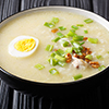 Hot Arroz Caldo traditional rice soup with chicken, vegetables and egg close-up in a bowl on the tab