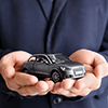 Male insurance agent holding toy car on grey background, closeup