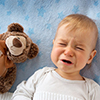 One year old baby lying in bed holding a plush teddy bear