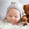 Sweet baby boy in bear overall, sleeping in bed with teddy bear stuffed toys, winter landscape behin