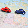Miniature red and blue toy cars driving in tandem on a map of canada