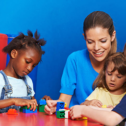 Children and nursery teacher building with blocks in kindergarten