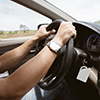 Cropped view of drivers arms and hands on steering wheel, and dashboard