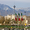 Three waving Iran flags in front of residential buildings, Milad Tower and Alborz Mountains in the c