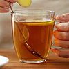 close up of woman adding ginger to tea cup with lemon and honey