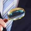 Midsection of person in suit examining documents with magnifying glass against black background