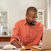 Mature man working on laptop while taking notes. Businessman working at home with computer while wri