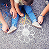 Close up of little girl and her parents drawing with chalks on the sidewalk