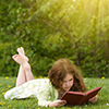 Young girl reading a book outdoors in summertime