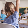 Small girl with hand up in classroom