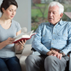 Senior care assistant reading book elderly man
