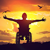 man in wheelchair stretching hands at sunset